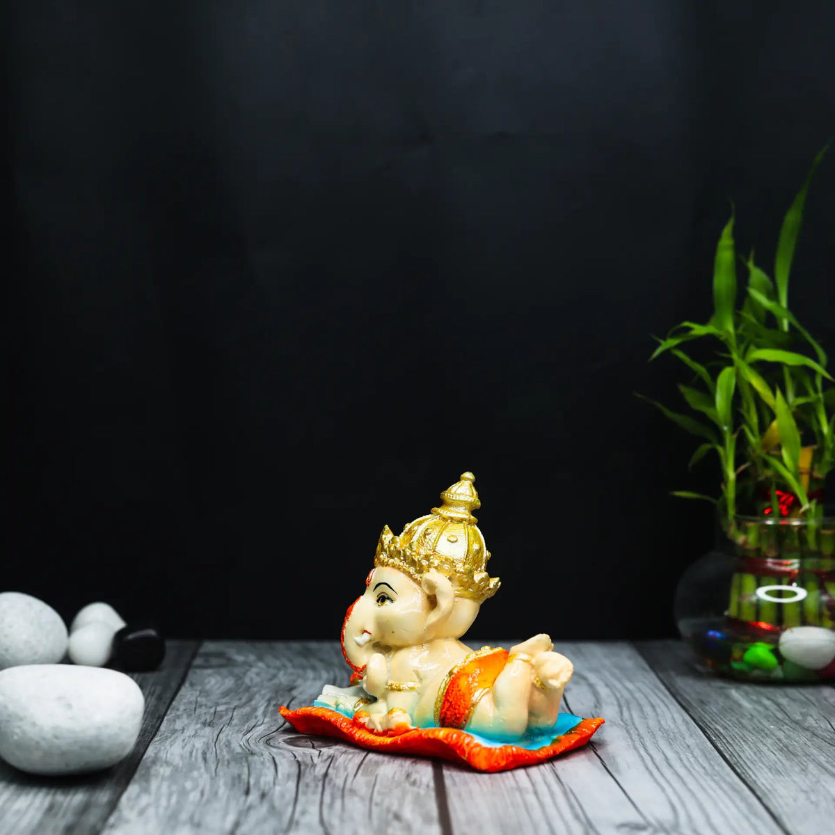 Aurance resin Bal Ganesha figurine reading the Ramayana, featuring gold accents on a wooden surface with bamboo.