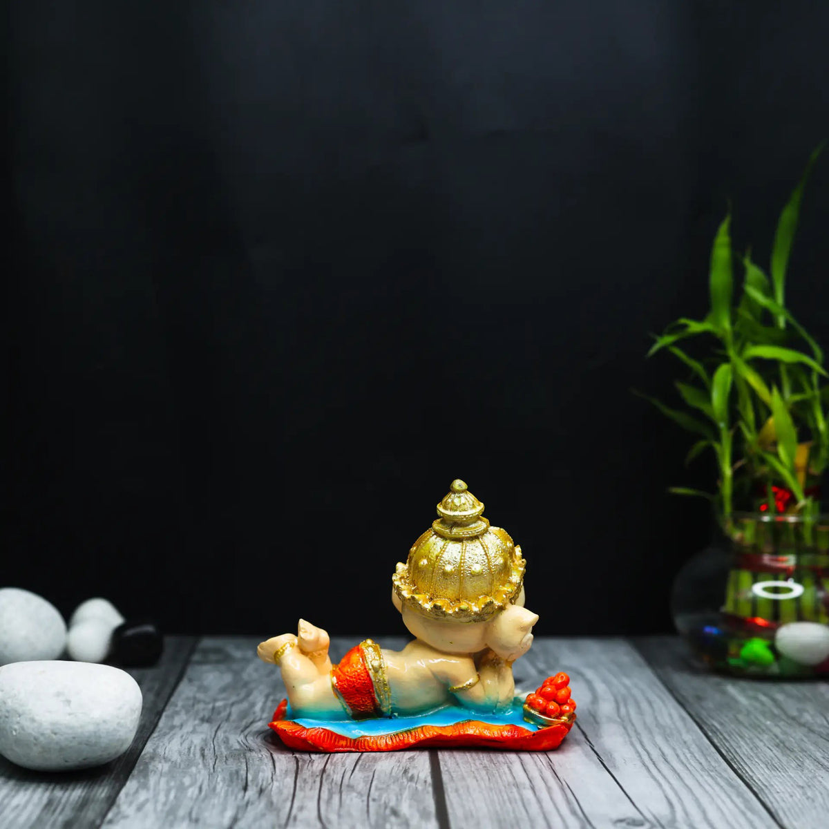 Aurance handcrafted resin Bal Ganesha figurine lying down and reading the Ramayana on a wooden surface with bamboo