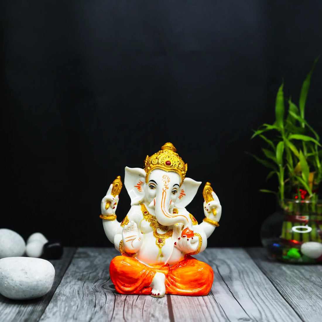 Aurance Ganesha idol with white body, gold crown, and orange dhoti, displayed on a wooden surface with bamboo decor.