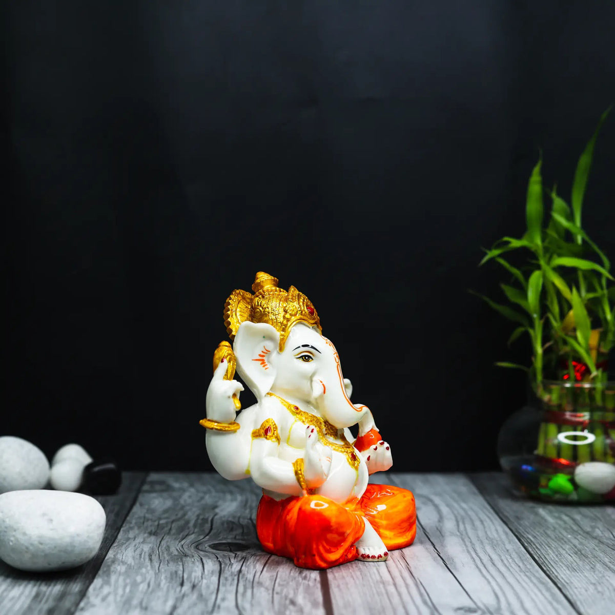 Aurance Ganesha statue with white body and orange dhoti, featuring gold accents, displayed on a wooden surface.
