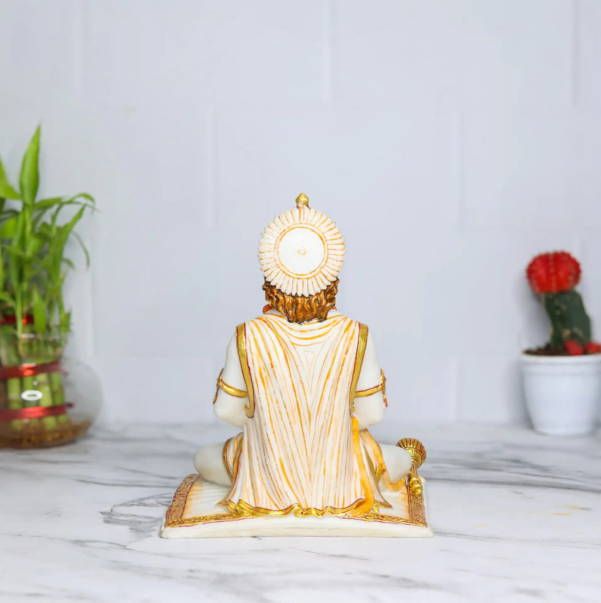 Rear view of an Aurance Lord Hanuman statue in a meditative sitting posture with a gada, set on a marble surface.