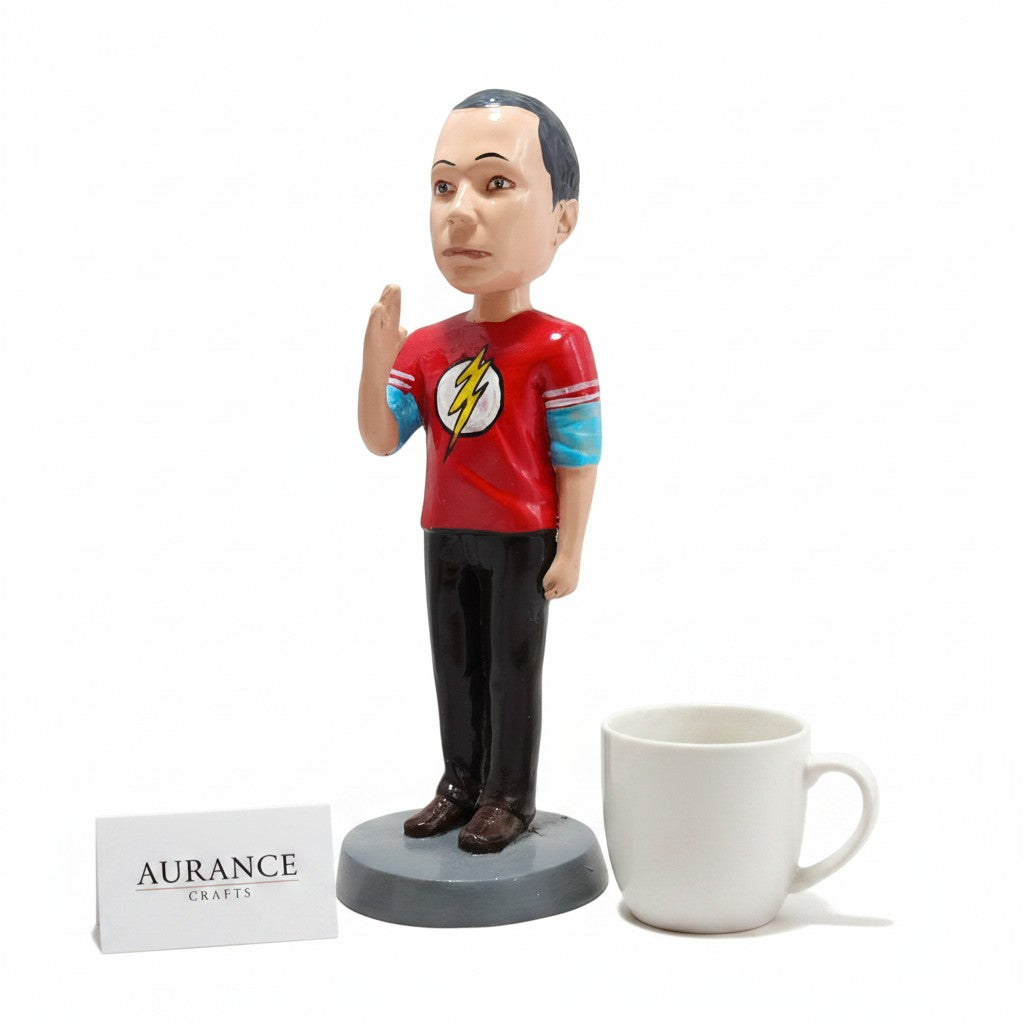 Aurance Sheldon Cooper resin bobblehead wearing a red Flash t-shirt, standing next to a white mug on a white background.