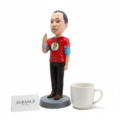 Aurance Sheldon Cooper resin bobblehead wearing a red Flash t-shirt, standing next to a white mug on a white background.